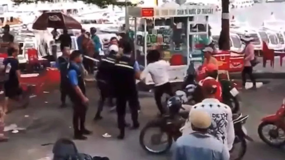 Người mặc áo thun trắng (tự xưng bảo vệ) dùng chân đá vào đầu khiến 1 người dân địa phương (trên 66 tuổi) xuất huyết não. Ảnh cắt từ clip