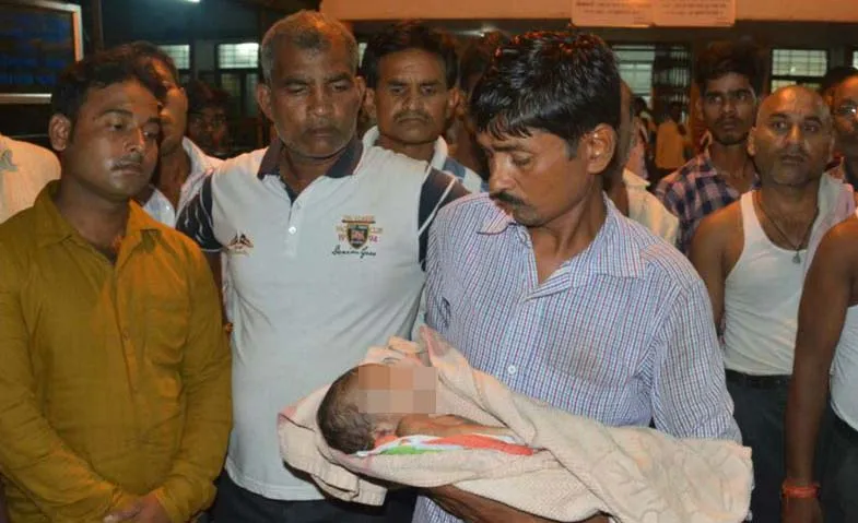 Một người đàn ông bế một trẻ nhi đã tử vong ở bên ngoài Bệnh viên Cao đẳng Y khoa Baba Raghav Das. Ảnh: AP