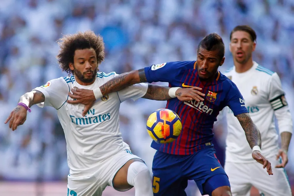 Marcelo (trái, Real Madrid) tranh bóng với Paulinho (Barcelona)