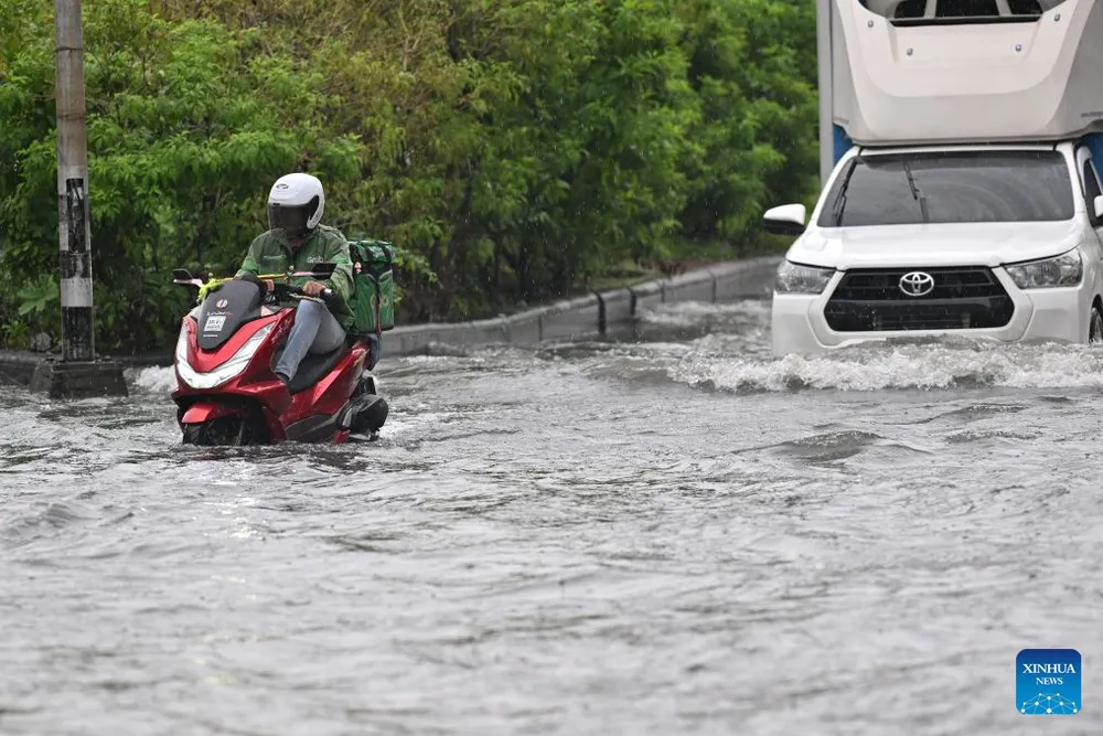 Một tài xế giao đồ ăn điều khiển xe máy băng qua vùng nước lũ ở Bangkok, Thái Lan, ngày 6-10. Ảnh: THX 