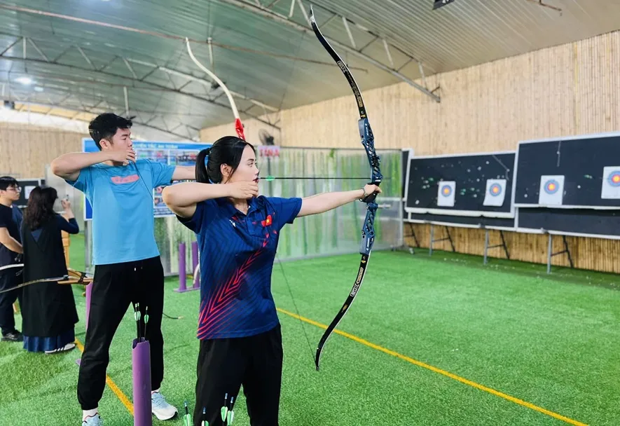 Ánh Nguyệt hướng dẫn Đức Phát làm quen với bắn cung để thêm hiểu hơn môn thể thao của mình. Ảnh: Đ.A.NGUYỆT