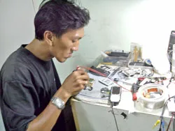 Anh Lương Viết Danh sửa lại chiếc điện thoại di động cũ bằng tay còn lại của mình. Ảnh: HỒ ĐAN