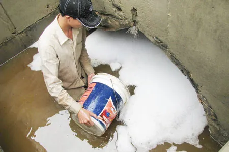 Một người dân đang múc dầu tràn trong miệng cống. Ảnh: Nguyên Khôi