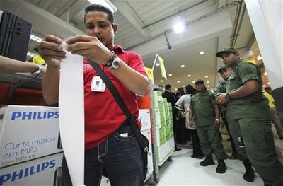 An officer of the Venezuela's consumer protection agency checks prices as soldiers look on at a supermarket, accused of raising prices, in Caracas, Monday, Jan. 11, 2009.
