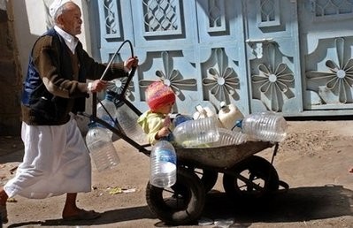 An elderly Yemeni man pushes a child sitting in a cart full of plastic containers as they head to fill them with drinking water in Sanaa