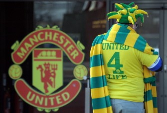 A street pedlar sells green and yellow scarves (that are used by fans in protest over the ownership of the club by US business tycoon Malcolm Glazer) outside Manchester United's Old Trafford stadium in Manchester on March 2, 2010. AFP photo