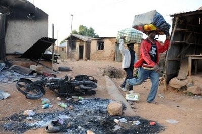 File photo shows residents carrying possessions past a burnt building following violent clashes in the town of Kuru Karama, 30 kilometres from Jos.