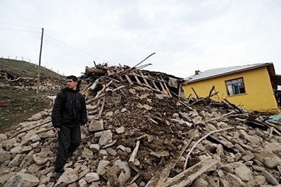 A man stands among debris in front of a destroyed house in the village of Okcular.