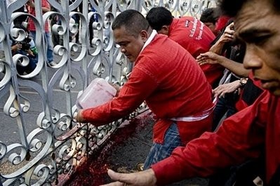 A red-shirted supporter of deposed Thai premier Thaksin Shinawatra pours a canister filled with human blood onto the gates of the Government House in Bangkok
