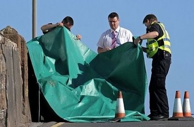 Police officers look a body at the scene of a shooting in Seascale, Cumbria