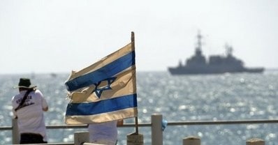 Two Israeli men stand near a national flag as they watch a navy vessel leave the Israeli port of Ashdod in southern Israel on June 5, 2010. (AFP file)