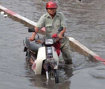 (Files) A man with a broken-down motorcycle wades through an inundated street after a heavy rain in HCMC (Photo: SGGP)