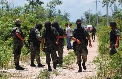 Mexican Army soldiers secure a dirt road after bodies were found nearby in several sinkholes in the resort city of Cancun, Mexico Friday June 18, 2010