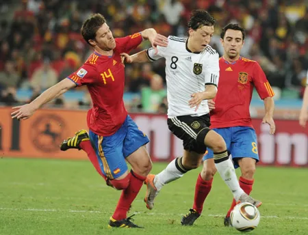 Tiền vệ Mesut Oezil (giữa, Đức) đi bóng trước 2 tiền vệ TBN Xabi Alonso (trái) và Xavi