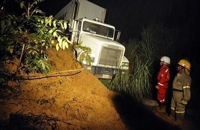 Two firefighters look a tractor-trailer trapped in a landslide on the road between Buga and Buenaventura in Colombia on December 4, 2010