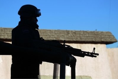 A federal police officer stands on a vehicle as he guards the area near a car where two people lie dead in the heavily guarded 'safe' zone, the PRONAF, in Ciudad Juarez, Mexico, Monday Dec. 13, 2010.