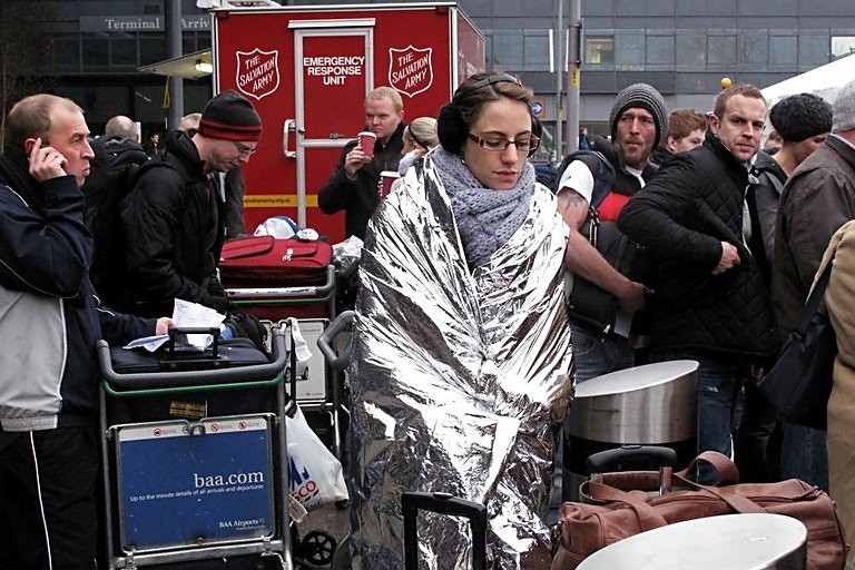 A woman keeps warm in a foil blanket, as she waits with other passengers for flight information, outside of Heathrow Airport's Terminal 3. AFP