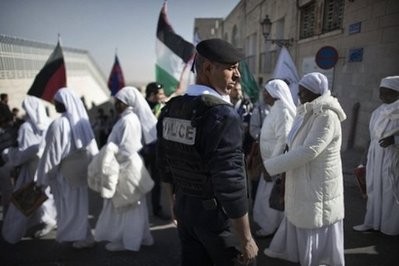 A Palestinian policeman stands guard as Nigerian worshippers cross a street near the Church of the Nativity in the Biblical West Bank city of Bethlehem