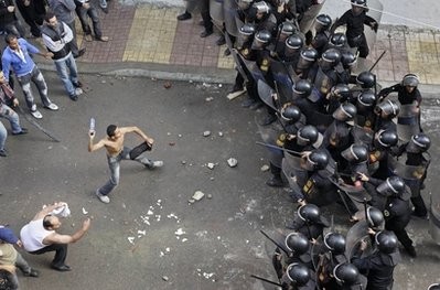 A Coptic protester, center-left, prepares to hurl an object at riot police during clashes between Coptic youths and riot police, who opened fire with rubber bullets and tear gas, in the streets outside the Saints Church and a neighboring hospital, in Alexandria, Egypt, Saturday, Jan. 1, 2011