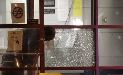 A Detroit police officer looks over one of the plate glass windows that was hit inside the precinct 6 building in northwest Detroit where a gunman walked into the police station and opened fire injuring police officers, Sunday, Jan. 23, 2011