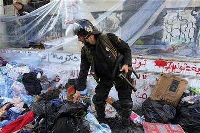 A Tunisian riot policeman searches through belongings of protesters after security forces stormed a protest camp outside the prime minister's office in Tunis January 28 2011
