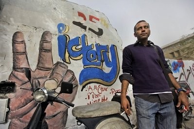In this photo taken Tuesday, Feb. 15, 2011, veteran labor activist and journalist Hossam el-Hamalawy is pictured next to graffiti celebrating the recent Egyptian uprising, on a street leading to Tahrir Square in downtown Cairo, Egypt.