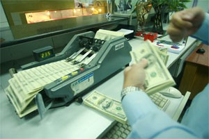 A cash teller puts a pile of US dollars into a cash counting machine at a HCMC-based branch of Asia Commercial Bank (Photo:Minh Tri)