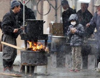 A boy (R) waits for boiled water to cook instant noodle outside a shelter in Sendai, in Miyagi prefecture on March 16, 2011.