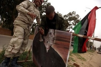 Fleeing Libyan rebels deface a poster of leader Moammer Khaddafi at the southern entrance of Benghazi.