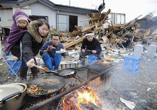 Tsunami survivors cook and eat in front of their damaged house Tuesday, March 15, 2011 in Ishinomaki in Miyagi Prefecture (state) after the area was badly damaged by Friday's massive earthquake and tsunami. (AP Photo/Kyodo News)
