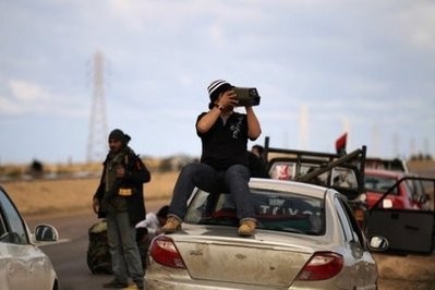 A Libyan rebel watches government troops several kilometres from the key city of Ajdabiya.
