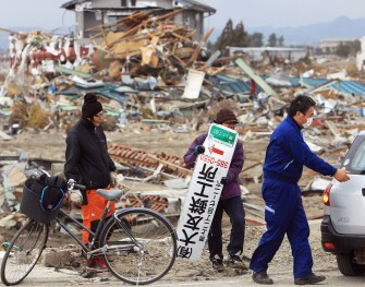 Residents recover a signboard of their father's factory amongst the debris after the elder was swept away by the tsunami in Natori, Miyagi prefecture on March 26, 2011. AFP