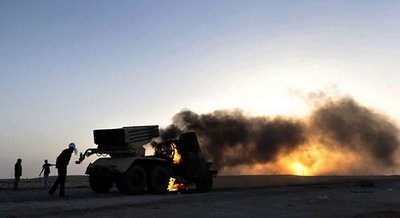 AFP - Libyan rebels walk past a burning multi-rocket launcher at sunset outside the oil rich town of Ras Lanuf.