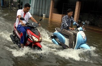 Thai men ride their motorbikes through flood waters following heavy rains in Thailand's southern city of Narathiwat on March 29, 2011. AFP