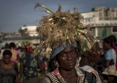 In this April 21, 2011 photo, a garlic vendor balances produce on her head as she walks through La Saline Market in Port-au-Prince, Haiti.