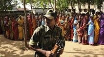 An Indian Border Security Force soldier keeps watch as voters wait in line at a polling station in Purulia