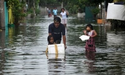 People walk through flood waters caused by a passing typhoon in Malabon, Metro Manila on June 21, 2011.