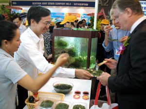 Two foreign visitors (on the right-hand side) try fresh seaweed at the Hai Nam Company booth at Vietfish on June 28, 2011 (Photo: Tuong Thuy)