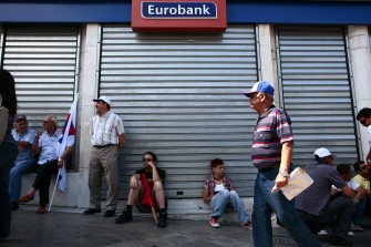 AFP - People sit in front of a closed bank in Athens on June 28, 2011 during a 24-hour general strike.