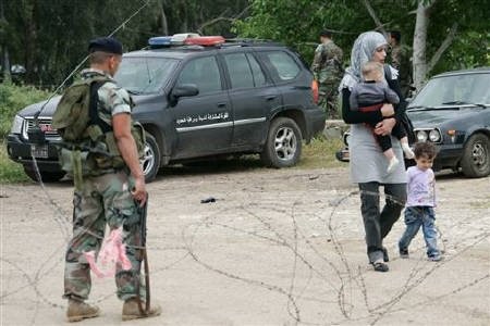 A woman from the Syrian border town of Tel Kelakh walks with her children past a Lebanese soldier standing guard at the border as she arrives in the northern Lebanese town of Wadi Khaled April 29, 2011