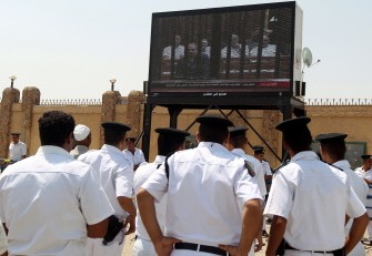 Egyptian policemen look at footage of former interior minister Habib al-Adly on a screen erected outside the Cairo Criminal Court on August 4, 2011