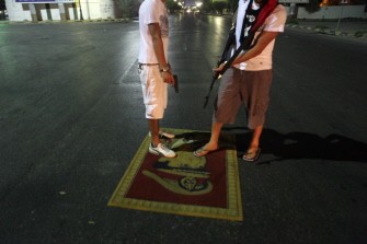 Libyan rebels step on a wall carpet depicting Moammer Khaddafi in a street of Tripoli early on August 24, 2011.