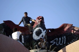 Libyan rebels take souvenir pictures on top of a broze falcon erected on the roof of one of ousted Libyan Leader Moammer Kadhafi Bab al-Aziziyah buildings in the capital Tripoli on September 12, 2011.
