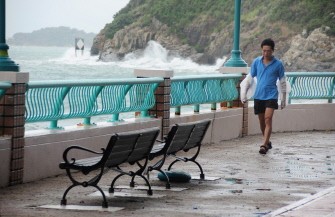 A resident walks along an oceanside prominade as waves caused by nearby Typhoon Nesat crash against the coast in Hong Kong on September 29, 2011