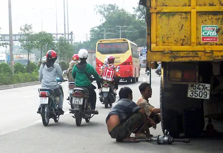 Vá vỏ xe ô tô trên quốc lộ 1A gần Đại học Nông Lâm TPHCM, gây cản trở lưu thông.