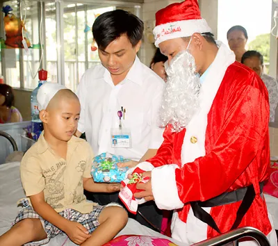 Ông Lê Minh Hiển (áo trắng) cán bộ phụ trách đơn vị Y xã hội Bệnh viện Chợ Rẫy trao quà Giáng sinh cho bệnh nhi nghèo. Qua hơn 3 năm thành lập, đơn vị Y xã hội đã hỗ trợ gần 5.000 lượt bệnh nhân cơ nhỡ có điều kiện chữa trị bệnh.