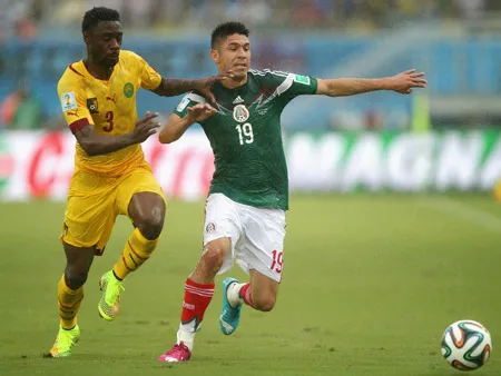 Oribe Peralta (phải, Mexico) vượt qua hậu vệ Djeugoue của Cameroon.