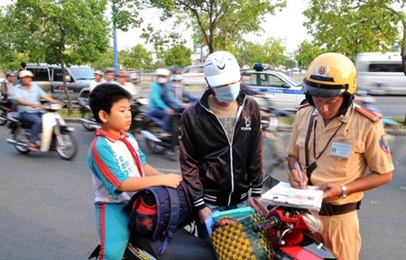 A policeman fines a parent for not making her son wear a helmet. With the new school year approaching, police in Ha Noi have called for co-operation from schools to crack down on students who ride electric bikes without wearing helmets. — VNA/VNS Photo An Hieu