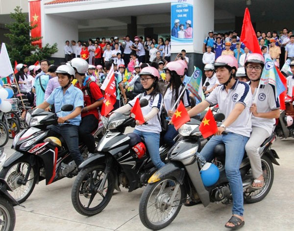 Students with standard helmets drive motorcycles and electricity bikes along streets in the city to call for people’s awareness of traffic regulation. (Photo:SGGP)
