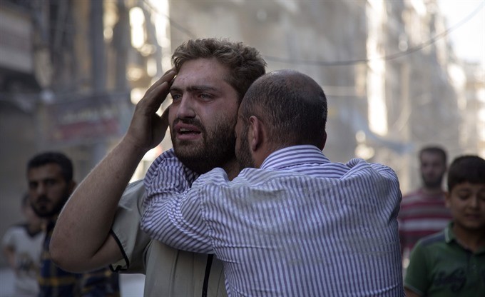Syrians react as the bodies of children are pulled from the rubble of a budling following government forces air strikes in the rebel held neighbourhood of Al-Shaar in Aleppo on September 27. - AFP/VNA Photo